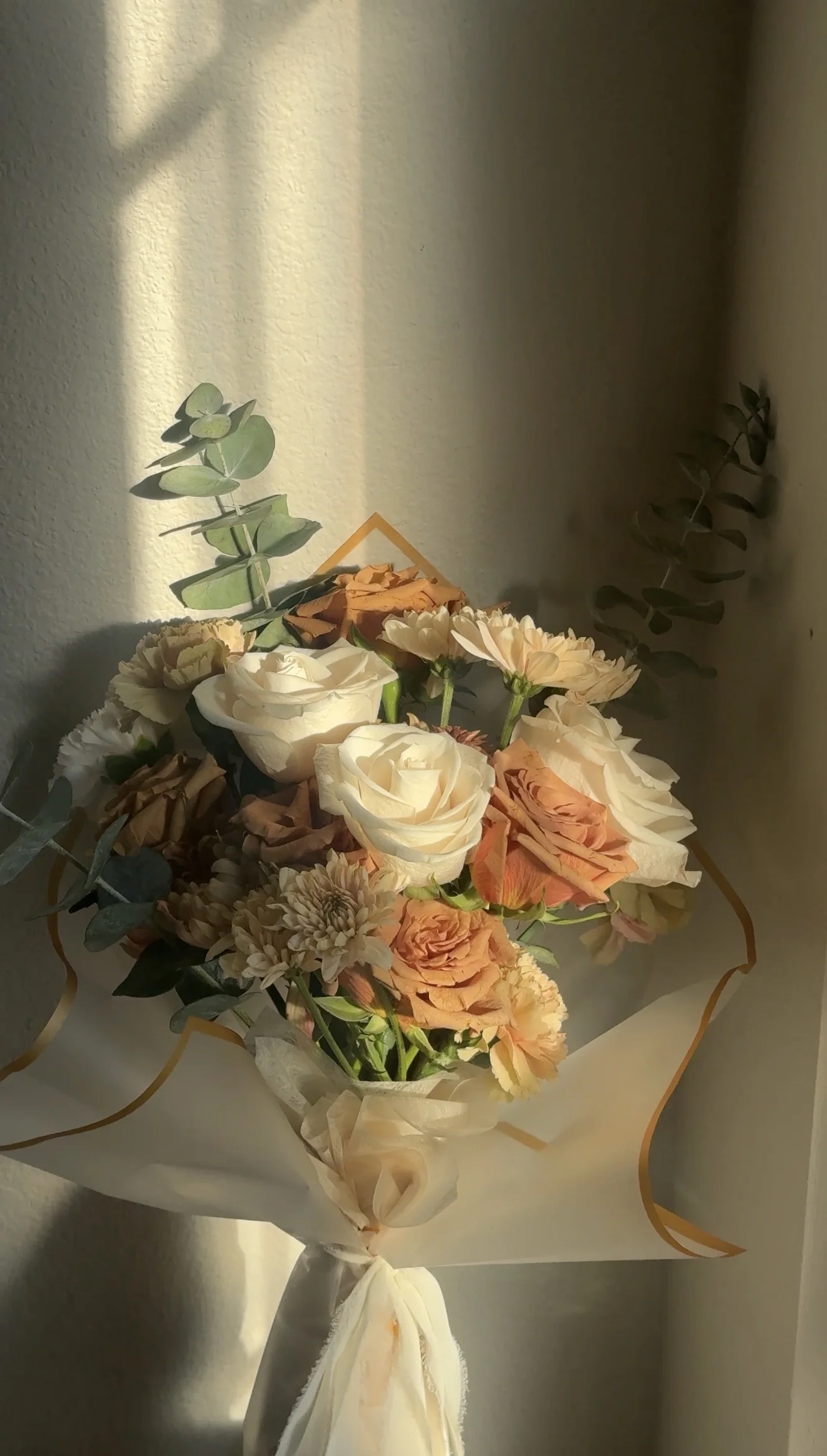 A close view of cream and peach roses with eucalyptus in a wrapped bouquet