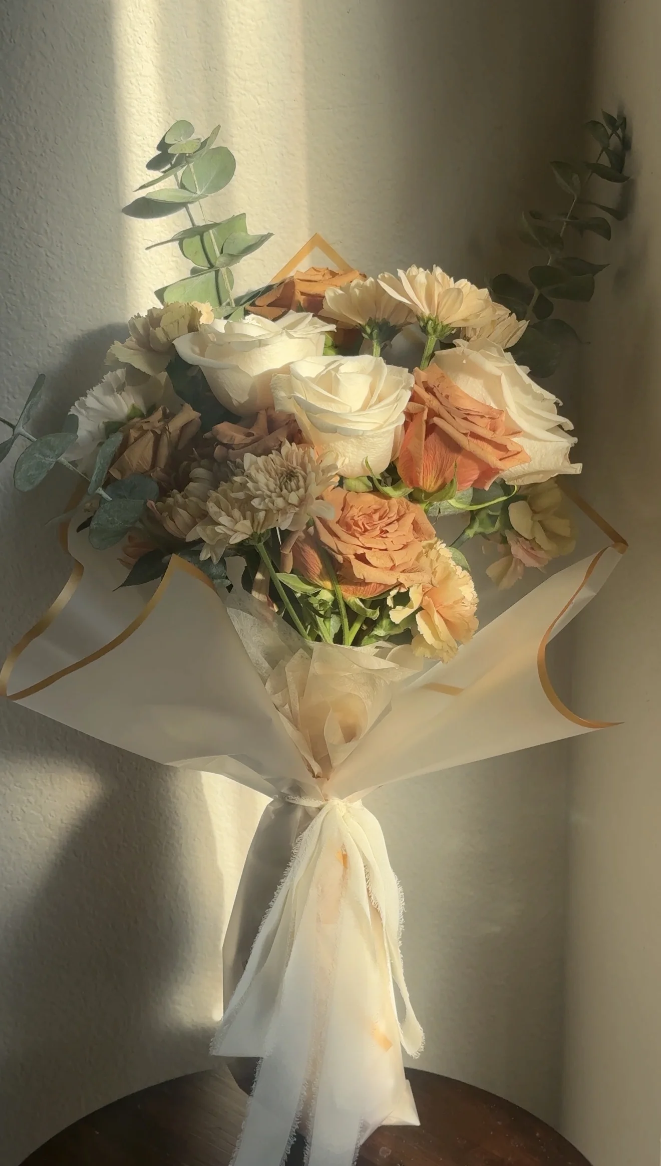 Cream and peach roses with eucalyptus, wrapped and tied with a cream ribbon