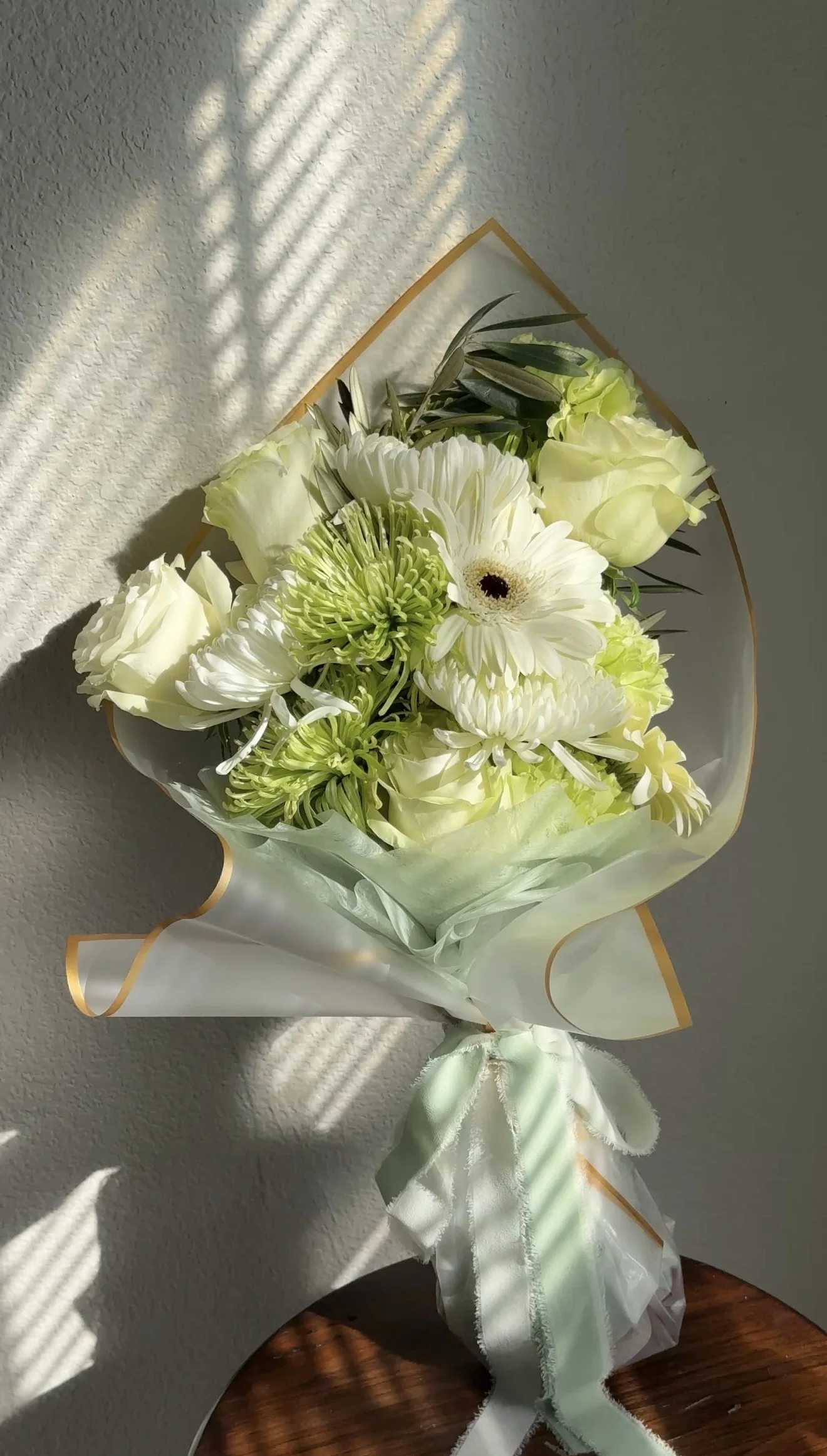 White and pale green flowers wrapped in paper with a soft green ribbon